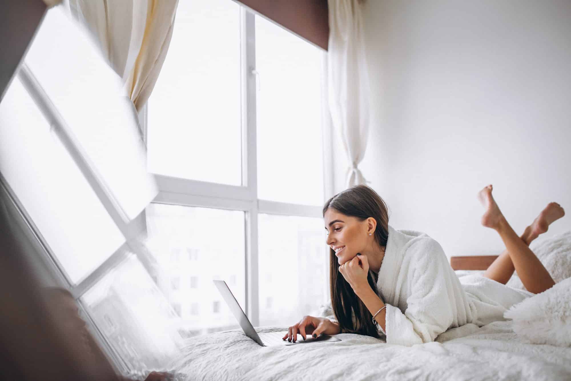 Designing Peace in Your Luminous, Large Floor Plan - a young woman working on her computer in bed.