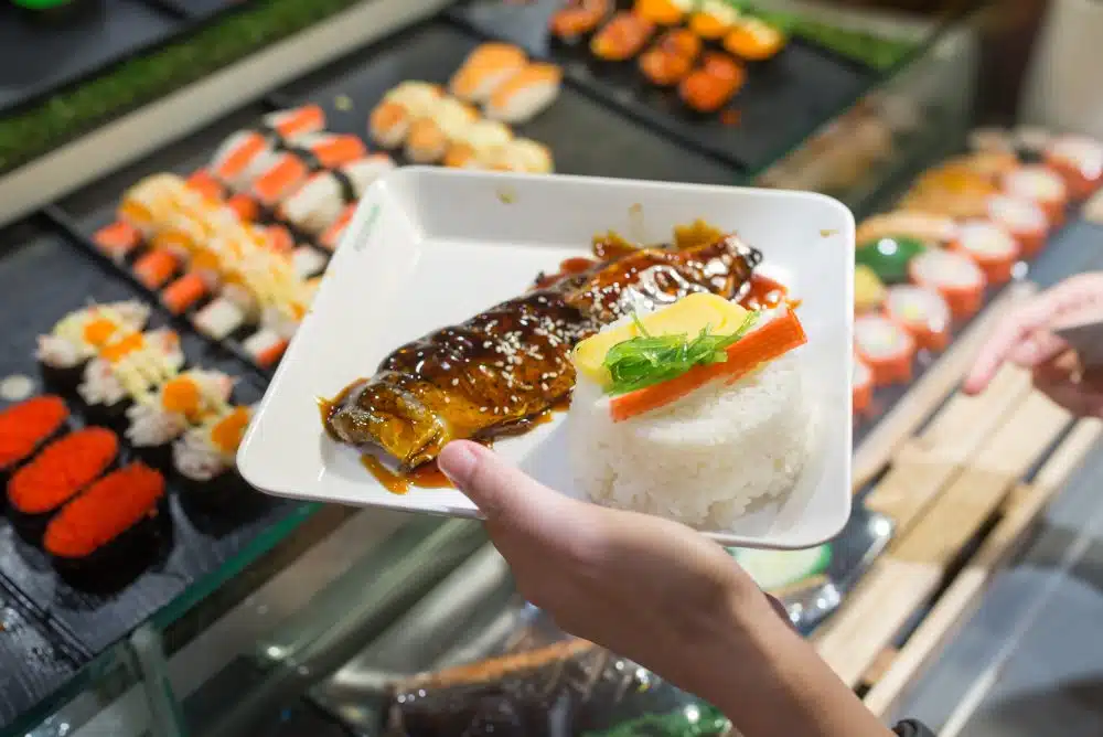 Walkable Dining Options Near Highland Apartments - Close-up of a plate with grilled fish, rice, and sushi rolls at a revolving sushi bar in Austin.