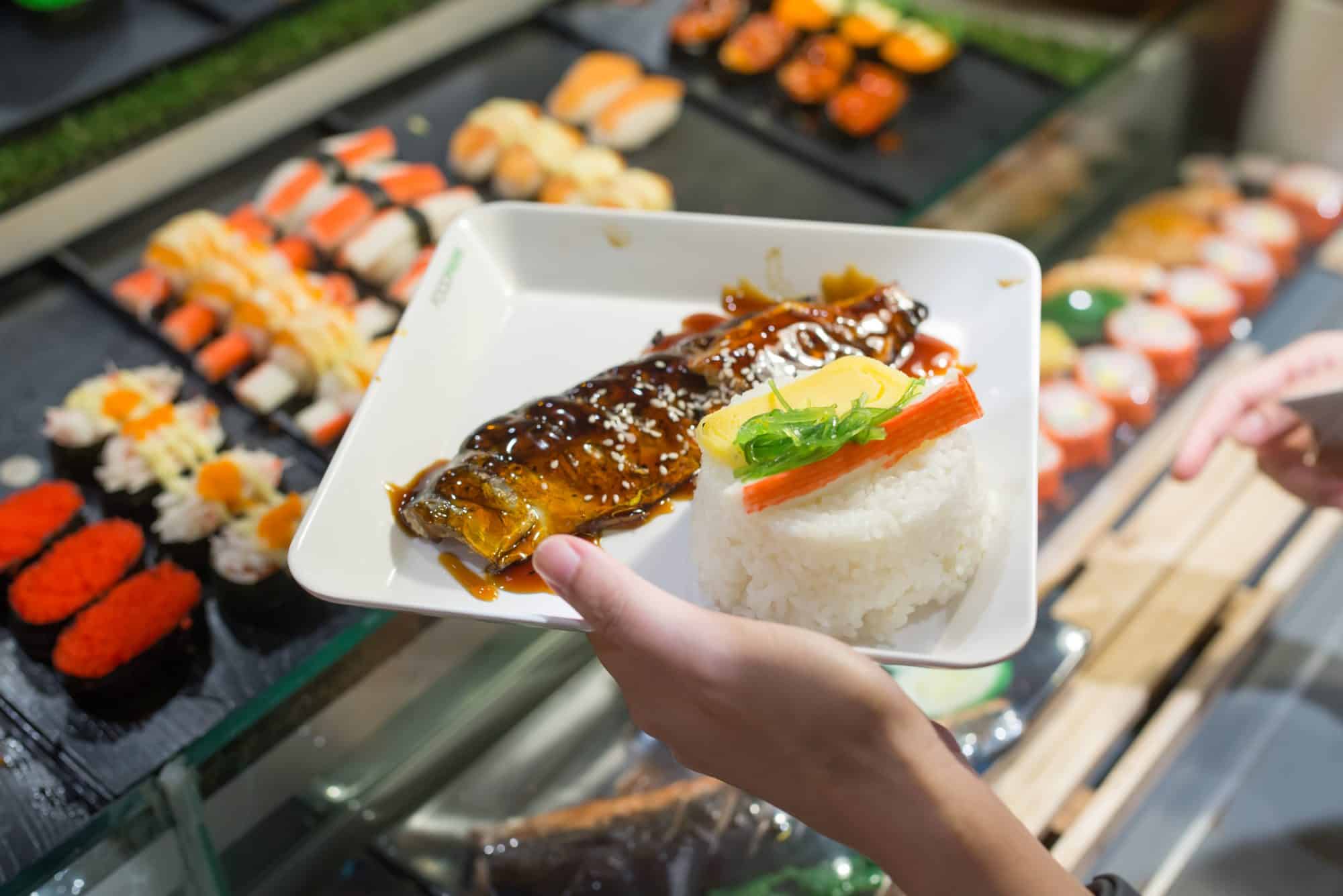 Walkable Dining Options Near Highland Apartments - Close-up of a plate with grilled fish, rice, and sushi rolls at a revolving sushi bar in Austin.